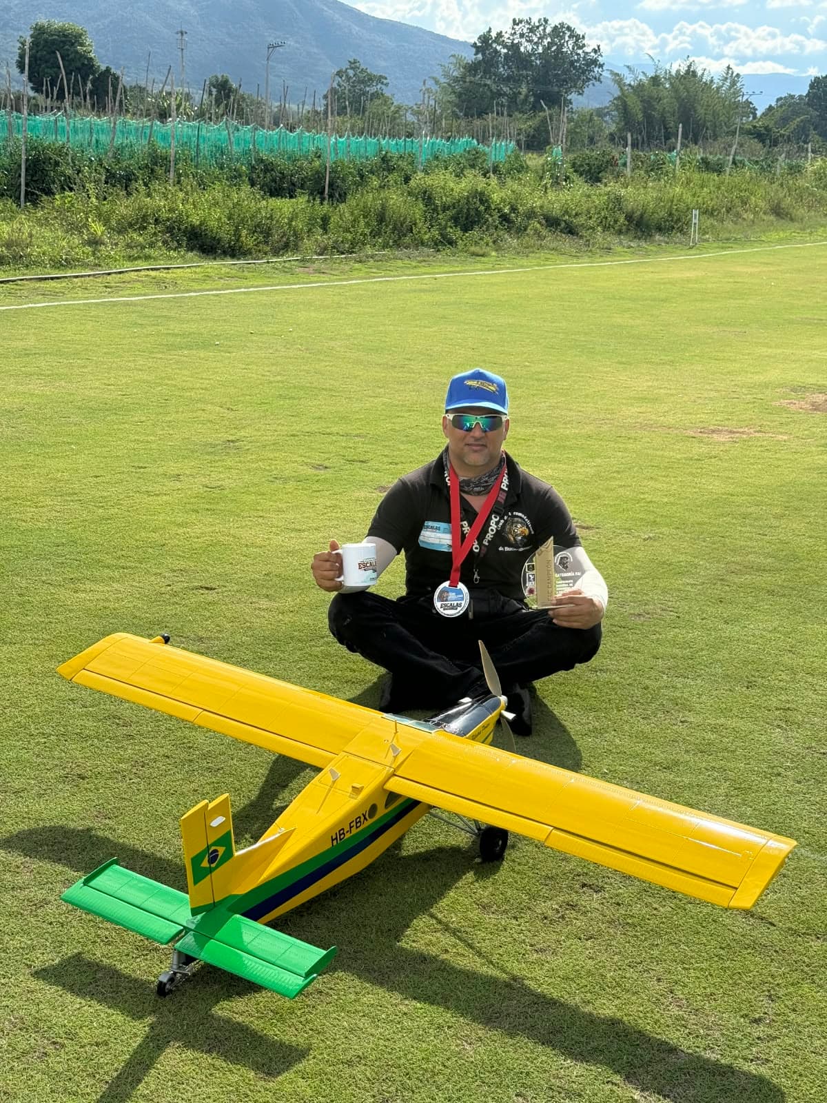 Dany Tovar sentado en la pista con su medalla y su trofeo, detrás de un avión amarillo a escala.